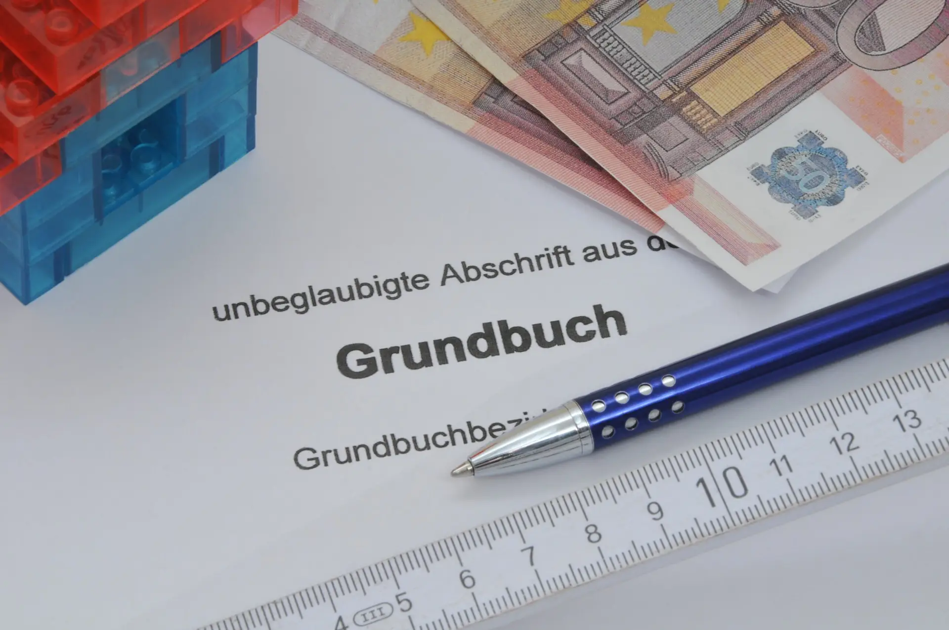 Ein Grundbuchauszug mit Euro-Scheinen, einem Stift und einem kleinen Hausmodell. Symbolbild für den sicheren Immobilienverkauf in Berlin.