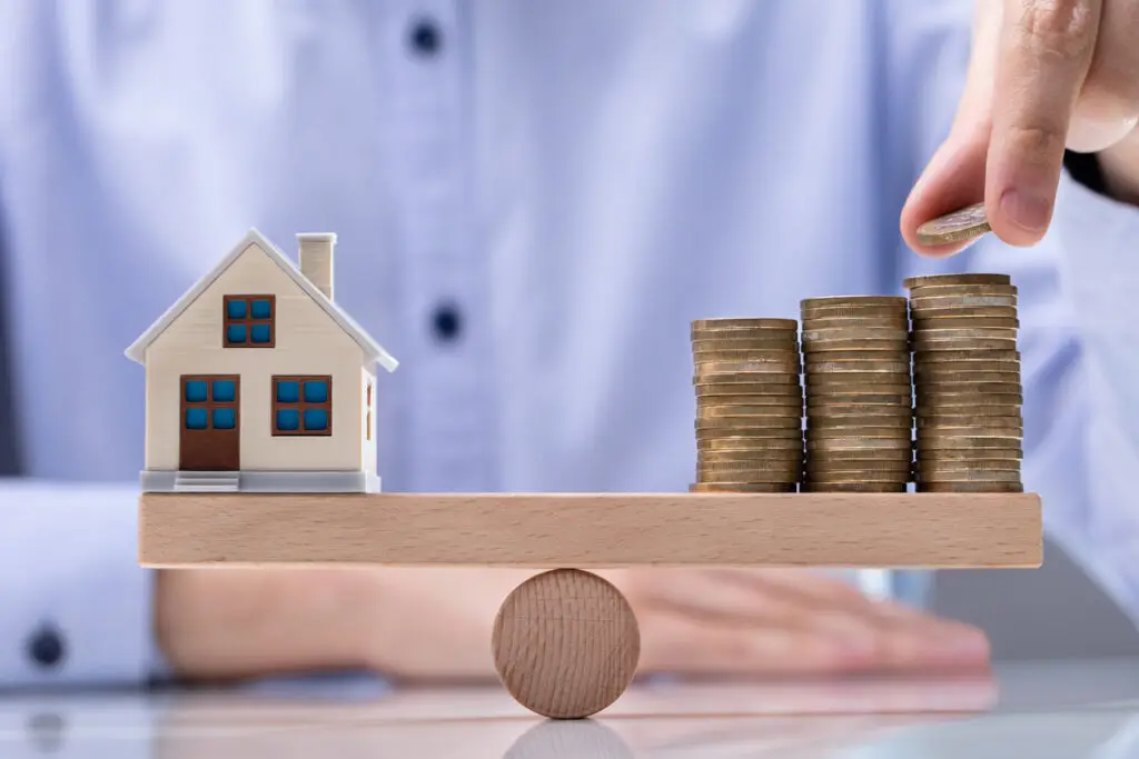 Featurefot: Männerhand legt Münze auf den Stapel Münzen und Modellhaus über Wippe