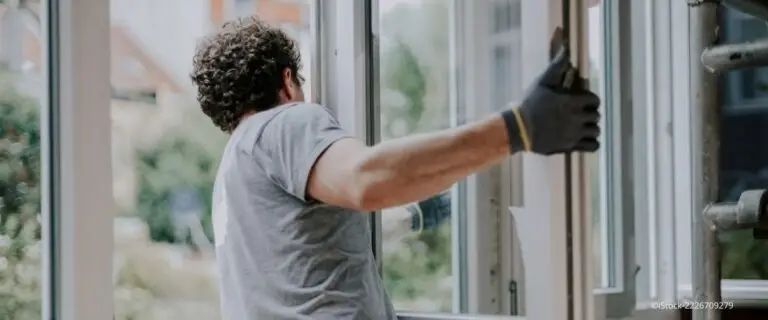Fenster sanieren: Handwerker mit Arbeitshandschuhen baut ein großes Fenster in einem Wohnraum ein.