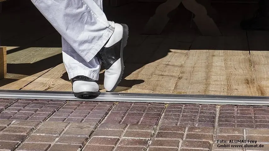 Person mit Golfkleidung steht lässig in einem stufenlosen Eingang von Terrasse in den Innenraum. Das symbolisiert den erhöhten Wohnkomfort durch barrierefreien Zugang.