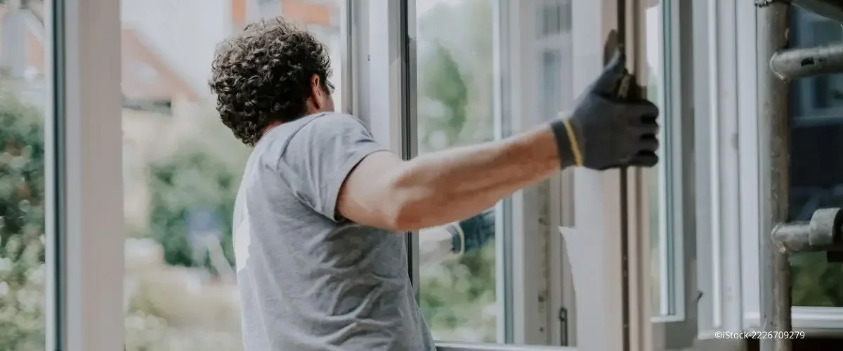 Fenster sanieren: Handwerker mit Arbeitshandschuhen baut ein großes Fenster in einem Wohnraum ein.