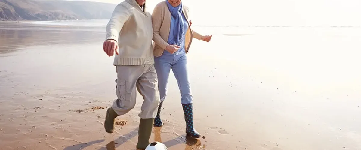 Senior Couple Playing Football On Winter Beach Having Fun